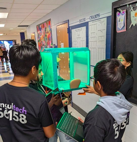 Students testing a glowing green climate-controlled chamber they built